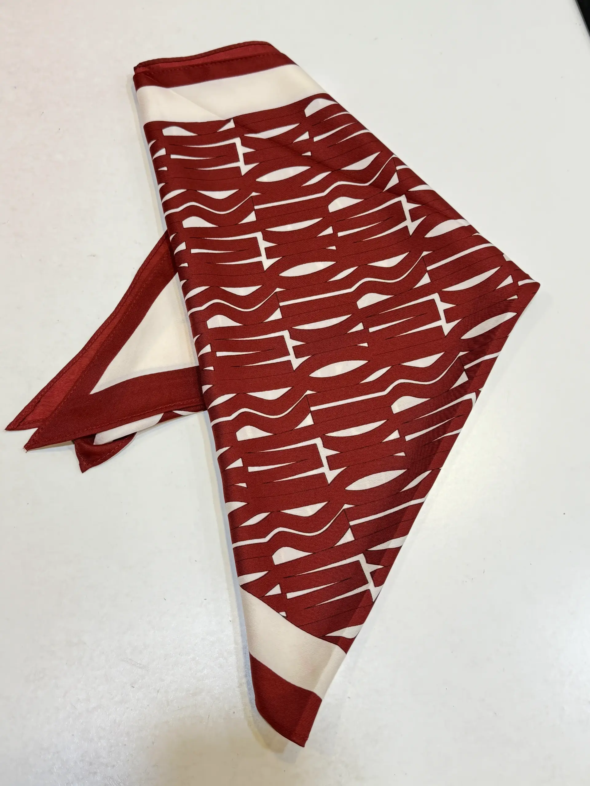 Pañuelo burdeos con estampado geométrico tipo tipografía en crudo y bordes combinados. Moderno y llamativo.